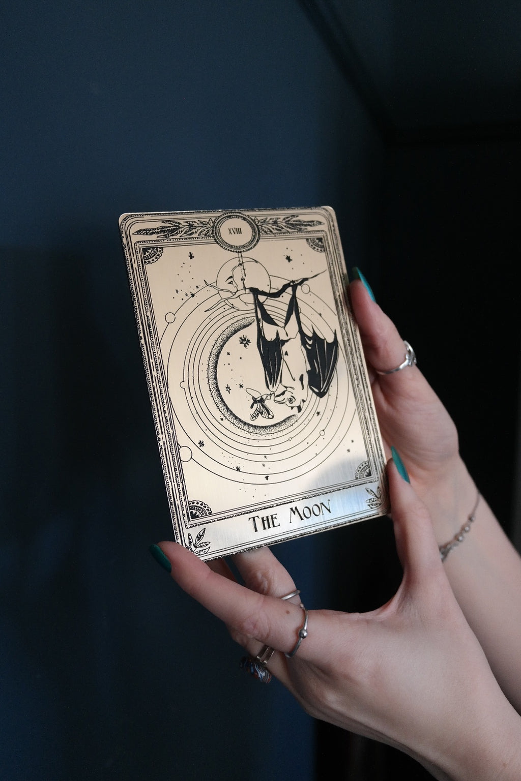 A decorative tarot card with a bat hanging under the moon.