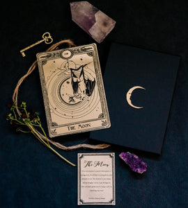 A gold tarot card with etched designs of the moon & a bat.