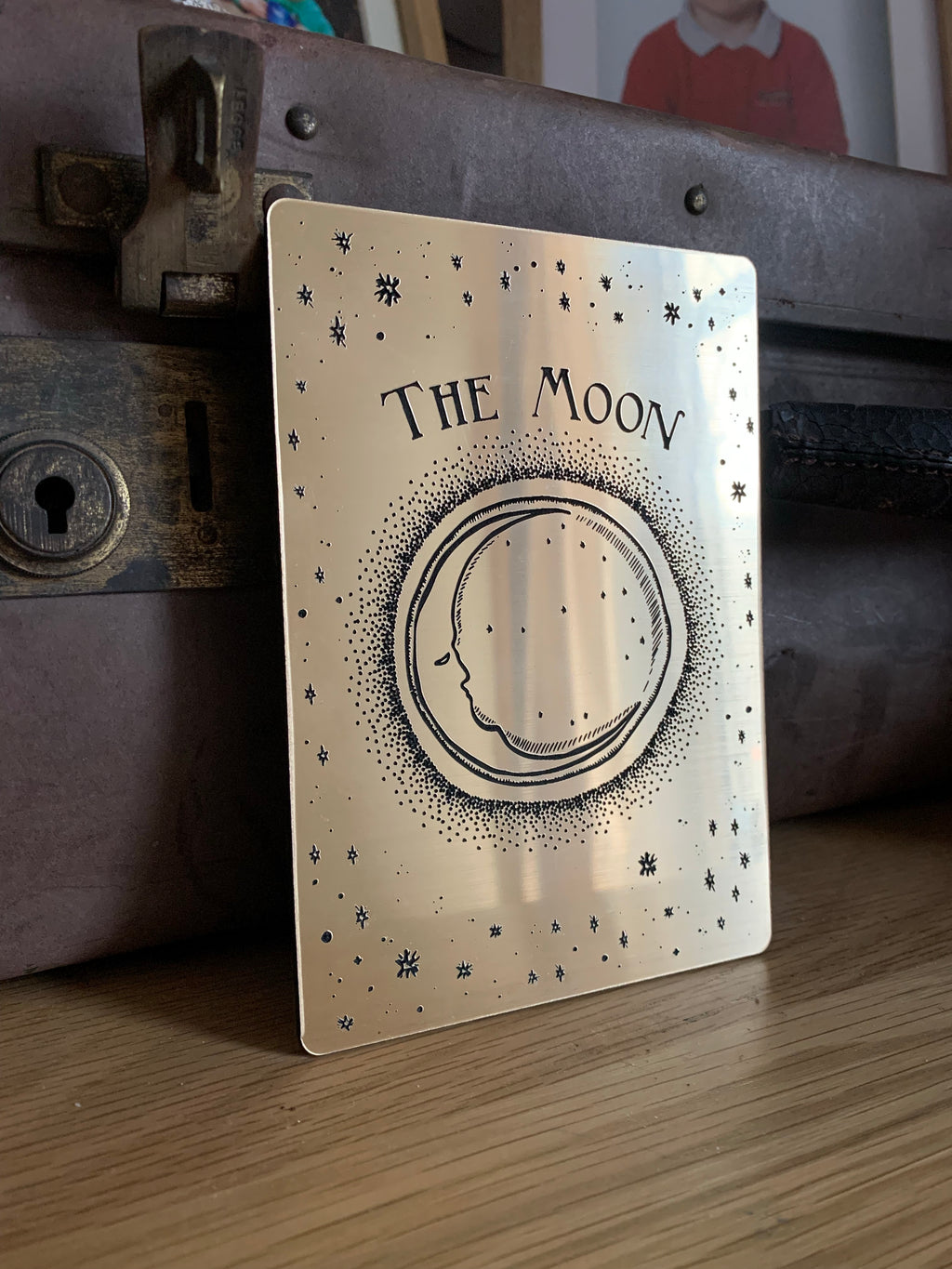 A decorative tarot card with etched design of a crescent moon, stars and the words 'the moon'